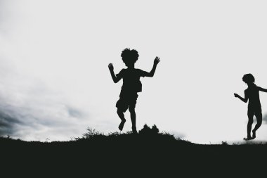 Sahilde kum bir uçurumun üzerinden atlama çocuklardan siluetleri