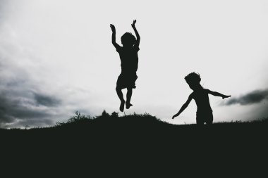 Sahilde kum bir uçurumun üzerinden atlama çocuklardan siluetleri