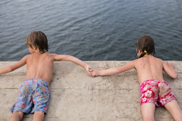 Gemelli fraterni abbronzatura sul ponte di legno al lago nella calda giornata estiva — Foto Stock