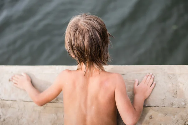 Niño pequeño bronceándose en la cubierta de madera en el lago en el caluroso día de verano — Foto de Stock