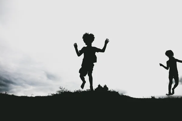 Siluetas de niños saltando desde un acantilado de arena en la playa —  Fotos de Stock