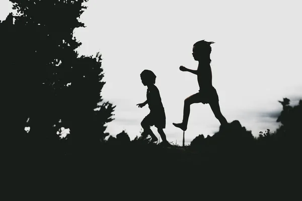 Silhouetten van kinderen springen van een rots zand op het strand — Stockfoto