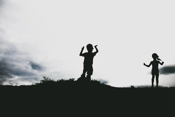 Silhouetten von Kindern, die von einer Sandklippe am Strand springen — Stockfoto