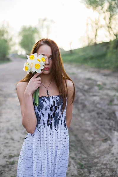 Jovem de cabelos vermelhos em vestido floral com buquê de narcisos — Fotografia de Stock