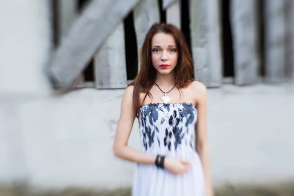 Rothaarige junge Dame in floralem Kleid in der Nähe eines verlassenen Gebäudes — Stockfoto