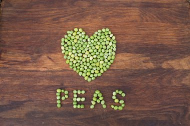 Taze yerel olarak yetiştirilen yeşil bezelye ahşap arka plan üzerinde yapılan kalp.