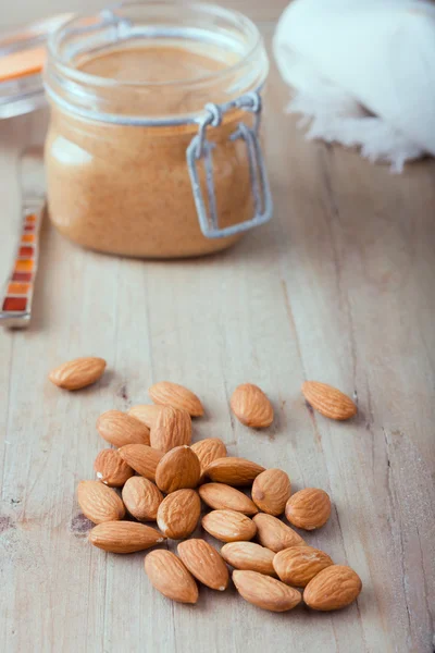 Almendras orgánicas crudas con mantequilla de almendras en el fondo —  Fotos de Stock