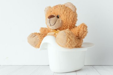 a teddy bear in a potty next to stack of diapers clipart