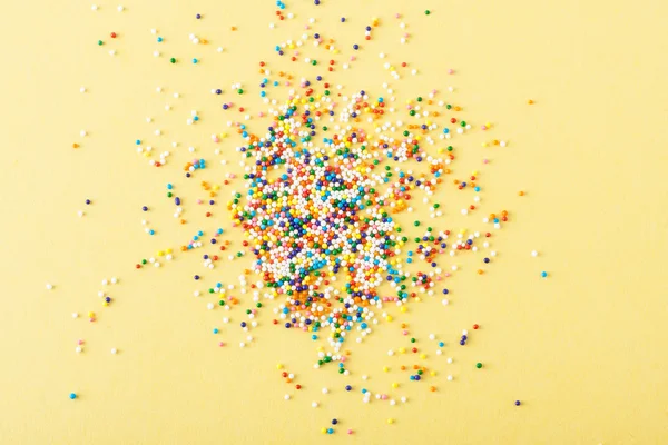 Colorful round sprinkles spilled on yellow background, isolated — Stock Photo, Image