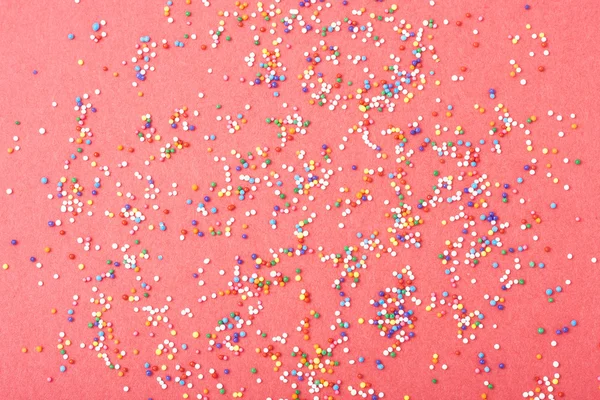 Colorful round sprinkles spilled on red background, isolated — Stock Photo, Image