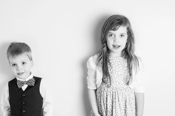 Black and white portrait of brother and sister standing against a wall — Stock Photo, Image