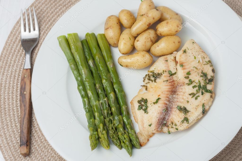 Cooked fish with parsley servied with asparagus and baby potatoes on