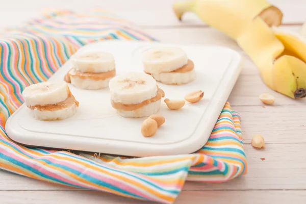 Банановые ломтики с арахисовым маслом на белой доске — стоковое фото
