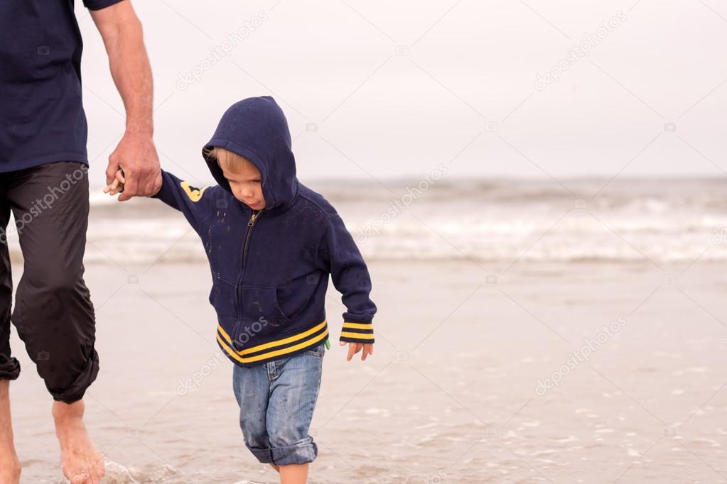 adorable obedient toddler boy walking on a beach holding hands with his father
