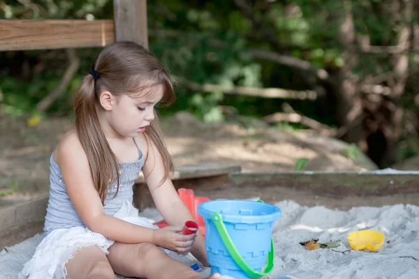 Adorable petite fille avec deux queues de porc jouant dans le bac à sable dans la cour ombragée — Photo