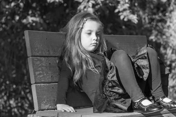 Tired or bored little girl sitting on a bench, black and white image — Stock Photo, Image