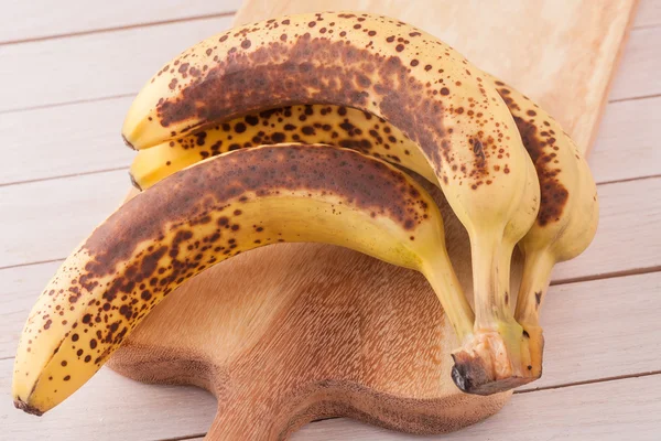 Um monte de bananas orgânicas muito maduras em uma tábua de corte de madeira — Fotografia de Stock