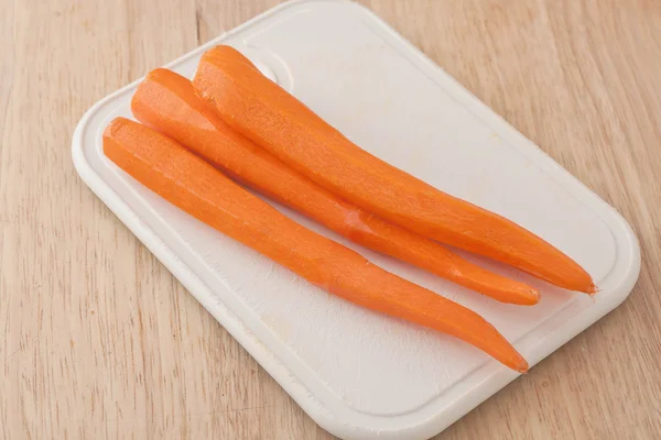 Fresh peeled long carrots on white chopping board — Stock Photo, Image