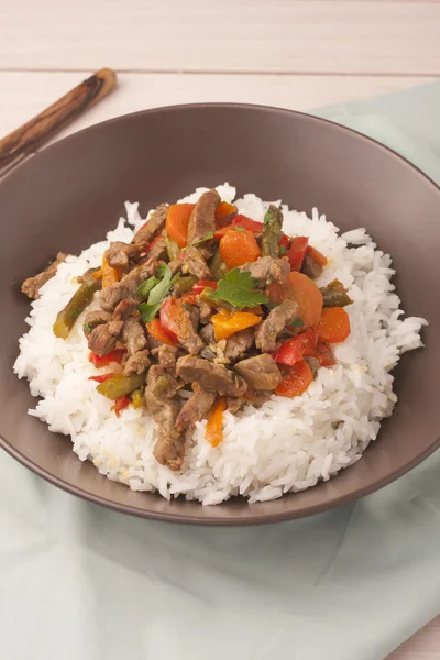 A brown bowl of white rice with stir fry beef with bell peppers, asparagus and carrots — Stock Photo, Image