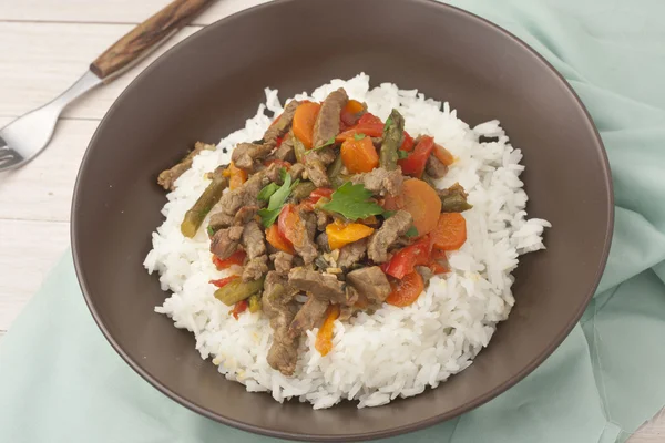 A brown bowl of white rice with stir fry beef with bell peppers, asparagus and carrots — Stock Photo, Image