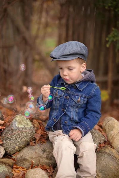 Un niño pequeño con una chaqueta de mezclilla soplando burbujas — Foto de Stock