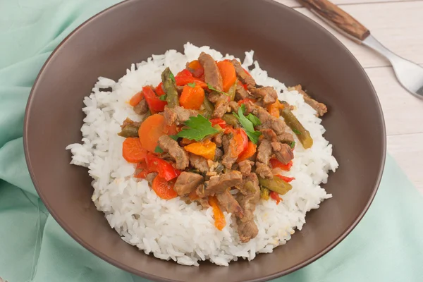 Eine braune Schüssel mit weißem Reis unter Rühren braten Rindfleisch mit Paprika, Spargel und Karotten — Stockfoto