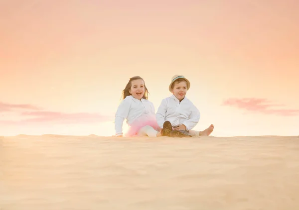 Two adorable little kids sitting on top of sand dune — Stock Photo, Image