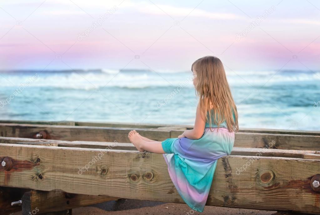 little girl sitting on a bench on a beach and looking at the ocean
