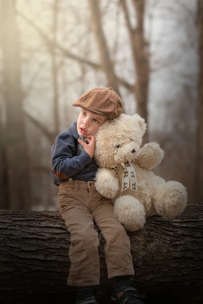 Menino sentado em uma árvore e abraçando um ursinho de pelúcia — Fotografia de Stock