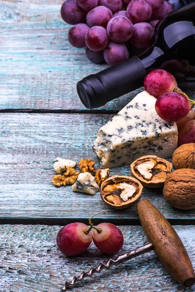 Red wine bottle, wine glass pink grapes, cheese, walnuts, corkscrew on wooden table background