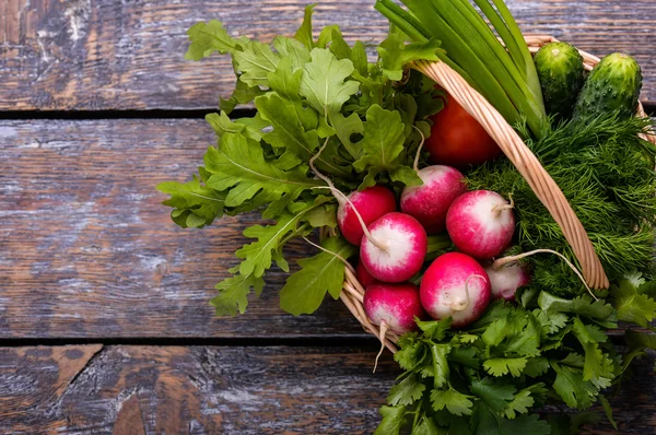 Весняні овочі та трави в кошику: редька, цибуля, петрушка, огірок на дерев'яному тлі . — стокове фото