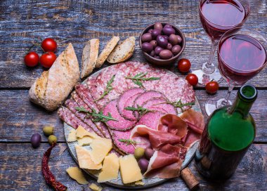 Kırmızı şarap bir bardak ve ürünler - peynir, sosis, salam, zeytin, domates, biber, bir dizi ekmek ahşap masa üzerinde arka plan