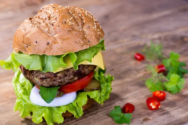 Großer Hamburger mit Rinderschnitzel und Gemüse auf Holzteller — Stockfoto