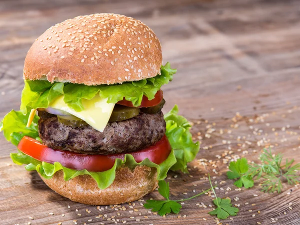 Großer Hamburger mit Rinderschnitzel und Gemüse auf Holzteller — Stockfoto