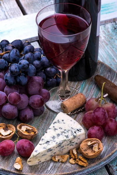 Botella de vino tinto, uvas, nueces y queso sobre fondo de madera —  Fotos de Stock