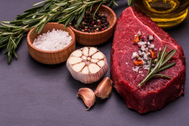 Ham sığır eti biftek, tuz, biber, sarımsak, biberiye kara tahta, arka plan üzerinde.