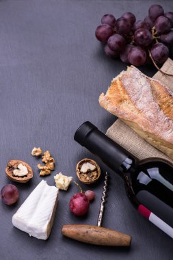 Kırmızı şarap şişesi, üzüm, ceviz ve siyah bir zemin üzerine peynir