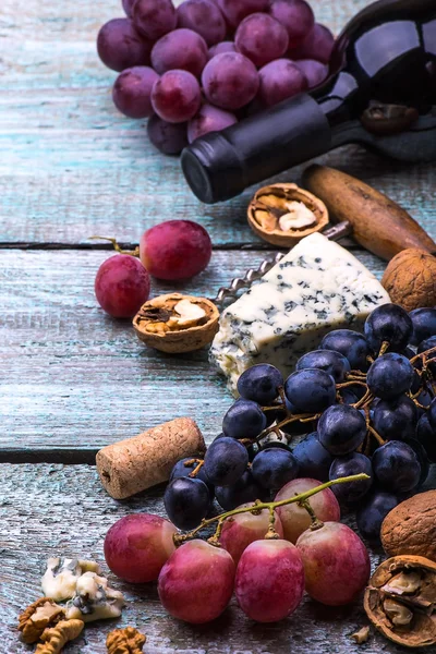 Botella de vino tinto, uvas, nueces y queso sobre fondo de madera —  Fotos de Stock