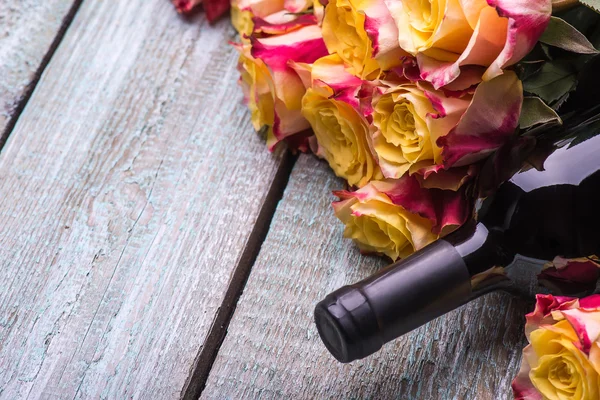 Red wine bottle, present box and flowers roses on wooden background