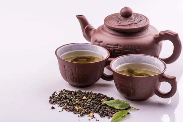 Zielona herbata w Pucharze i czajnik, płatki zielonej herbaty na Bambusowa Mata na białym tle — Zdjęcie stockowe