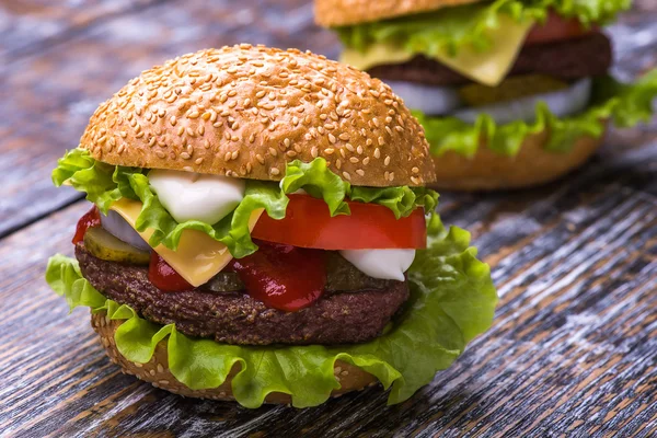 Hamburguesa con chuleta de res, verduras frescas: tomates, cebollas, lechuga, salsa y bollo con semillas de sésamo sobre un fondo de madera — Foto de Stock