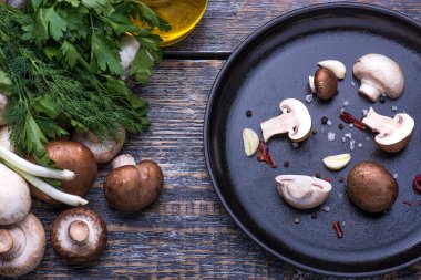 Mushrooms, parsley, dill, onion, olive oil, spices - ingredients for the preparation of mushroom dishes in a frying pan on a wooden background clipart