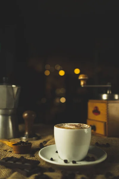 Bir fincan kahve, kapuçino. Kahve öğütücüsüyle, espresso makinesiyle ve çikolatayla güzel bir kompozisyon. Restoran ve kahve dükkanı. Güzel kremalı bokeh..