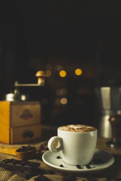 Bir fincan kahve, kapuçino. Kahve öğütücüsüyle, espresso makinesiyle ve çikolatayla güzel bir kompozisyon. Restoran ve kahve dükkanı. Güzel kremalı bokeh..