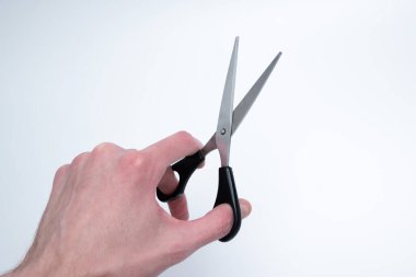 Temiz bir arkaplan karşısında siyah plastik saplı açık makas tutan insan eli, basitlik ve işlevselliği vurguluyor.