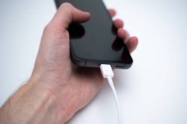 Bir el, modern teknolojinin gelişimini gösteren şarj kablosuna bağlı bir telefonu tutuyor..