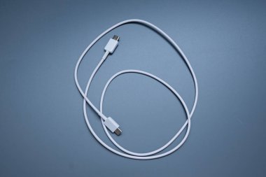 Beyaz USB kablosu mavi bir yüzeye sarılı, modern teknoloji cihazlarını bağlamak için uygun..