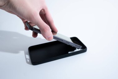 Siyah akıllı telefon ekran dışında dikey duruyor, siyah kapak beyaz masanın yanında yatıyor..