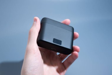 Beyaz arkaplanda USB-C portu ve göstergesi olan kablosuz kulaklıklar için sıkıştırılmış siyah şarj kutusu.