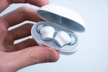 Beyaz kablosuz kulaklıklar şarj kutusu açık. Arka planda iki beyaz kulaklık görünüyor..